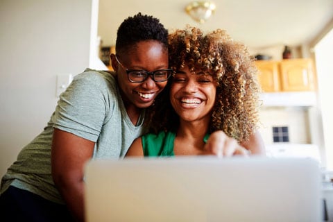 A smiling couple looking at an open laptop computer.